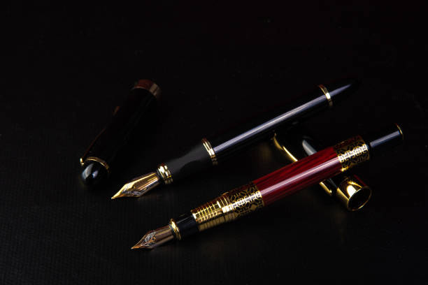 Image de deux stylos à plume un rouge et un noir détachée de leur capuchon sur un arrière-plan noir.