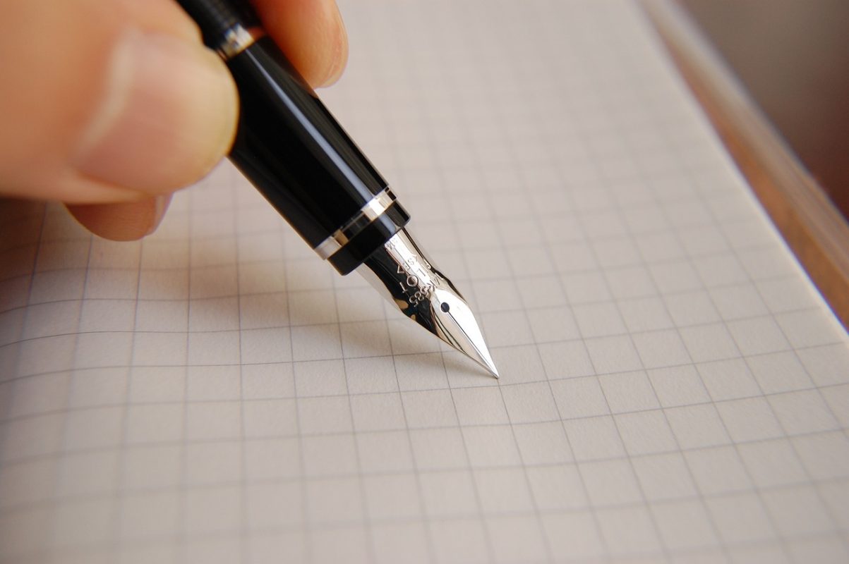 Image montrant un stylo à plume tenu par une main sur une feuille à petits carreaux.