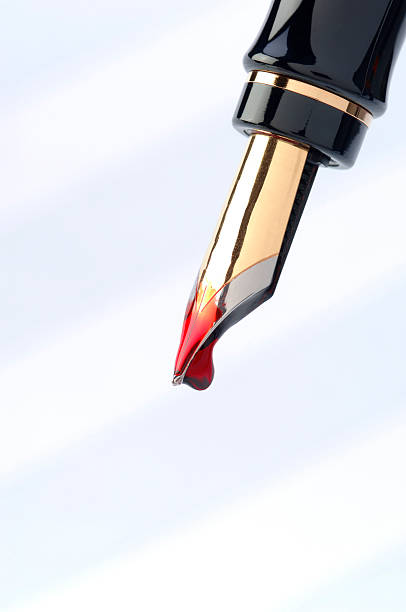 Une image de stylo à plume noir à détail dorée avec une goute d'encre rouge qui est sur le point de tomber.