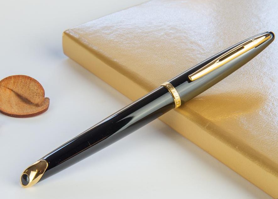 Image d'un stylo Waterman noir à détail doré poser sur un carnet beige.